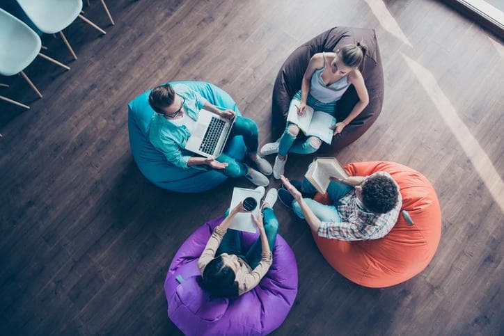 High top angle view of diversity stylish and modern hipster youngster sit in colorful armchairs on the wooden floor work together on the task