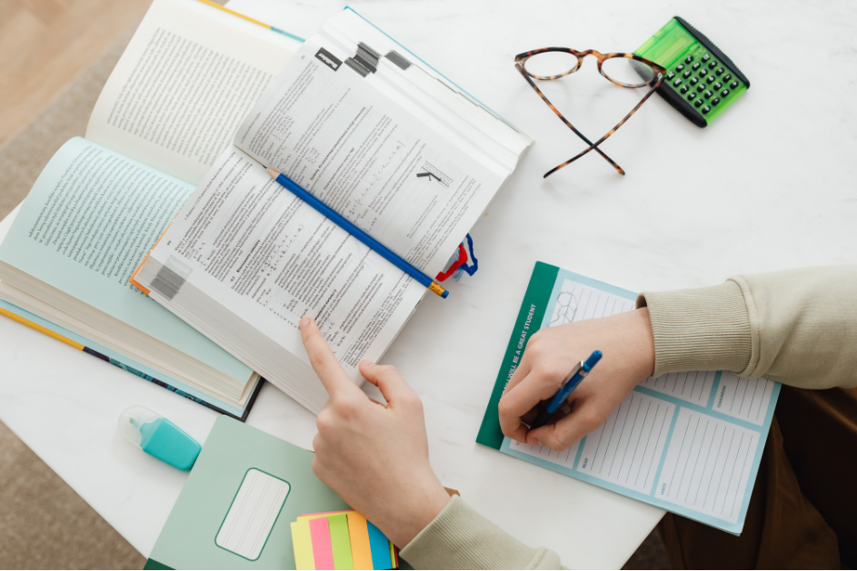 person taking notes with lots of books open on desk/ iStock